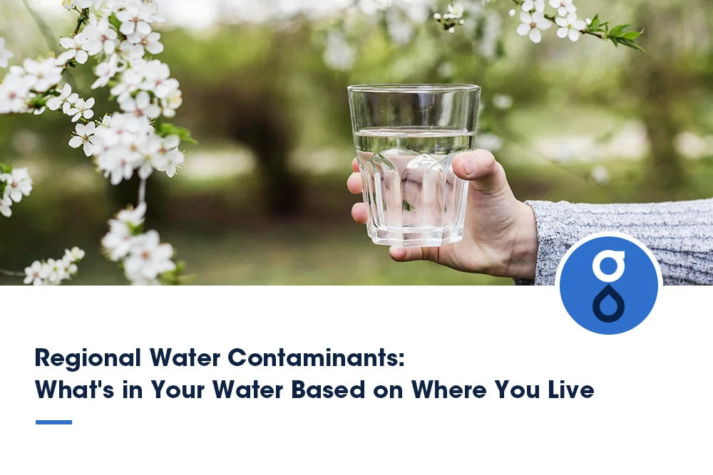 a hand holding a clear glass of water against a background of blooming white flowers, creating a spring or summer natural atmosphere. In the bottom right corner, there's a blue circular water droplet logo