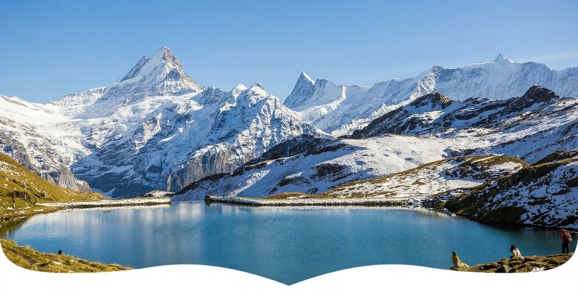 Lake surrounded by snow-capped mountains under a clear blue sky