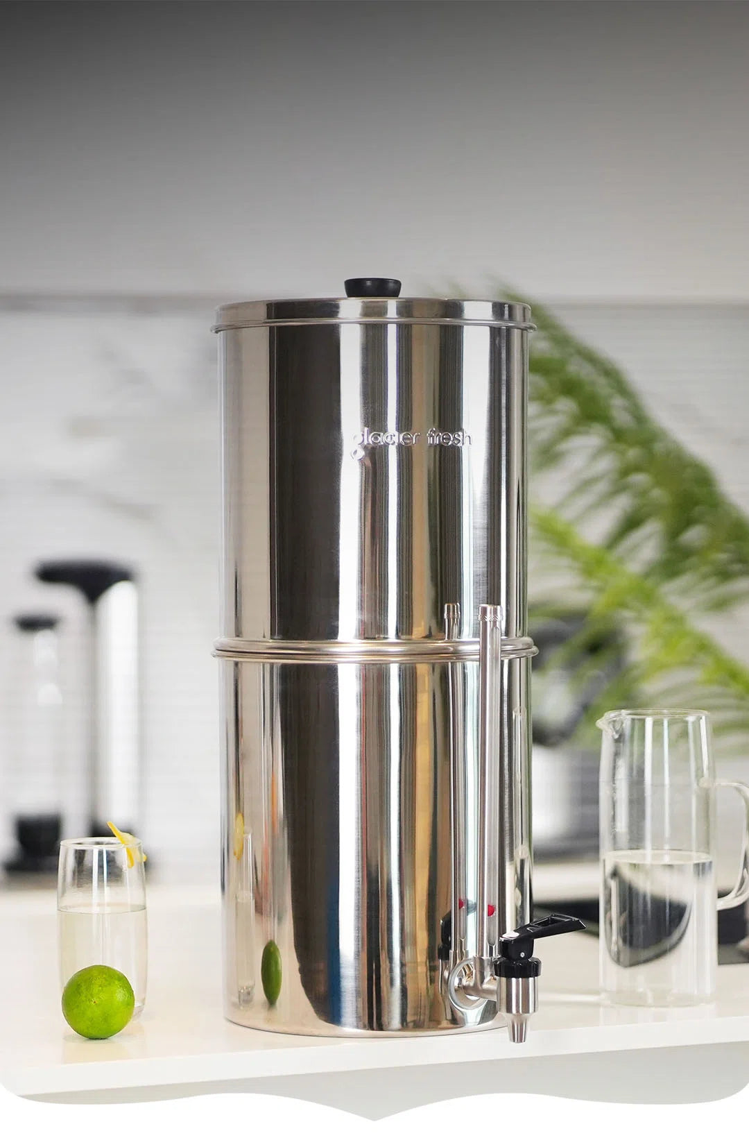 Stainless steel water filter on a kitchen counter with glasses and a lime.